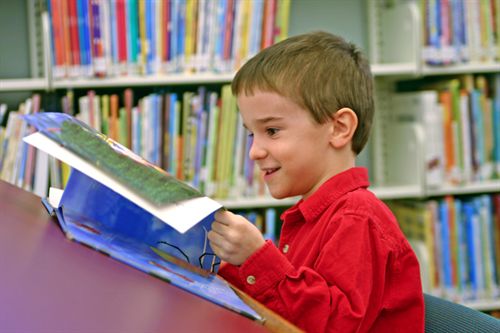 A child reading a picture book in the library.